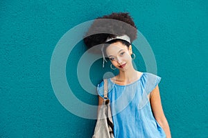 Happy young black woman standing and posing against blue wall in daylight