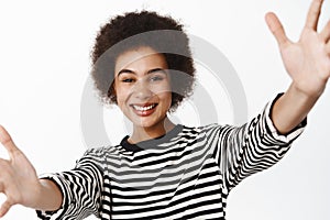 Happy young black woman stretching out arms, hugging, holding camera and smiling, taking selfie or video chat on mobile