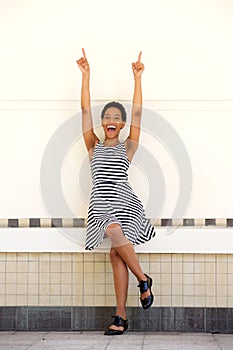 Happy young black woman in striped dress pointing fingers up