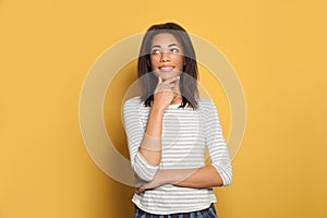 Happy young black woman student looking up and thinking on yellow background