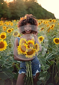 Happy young black woman walks in the sunflower field. Smiling dark-skinned girl with with a bouquet of sunflowers and