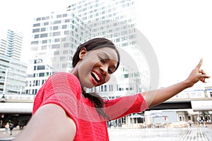 Happy young black woman taking selfie in the city and pointing to buildings