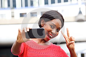 Happy young black woman taking selfie with peace hand sign in the city
