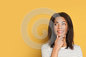Happy young black woman thinking on yellow background