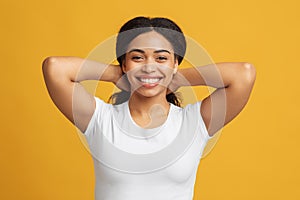 Happy young black woman touching and playing with her hair, looking and smiling to camera over yellow background
