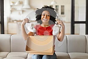 Happy young black woman unboxing parcel and holding up white sneakers