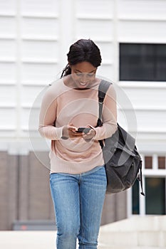 Happy young black woman walking and looking at cellphone