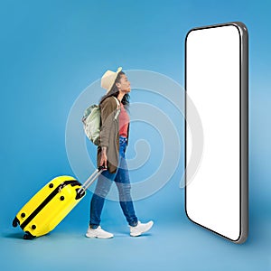 Happy young black woman walking with suitcase, checking smartphone screen