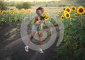 Happy young black woman walks in the sunflower field. Smiling dark-skinned girl with with a bouquet of sunflowers and