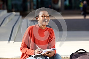Happy young black woman writing in book outside