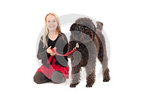 Happy young blonde girl holding black labradoodle on a red leash