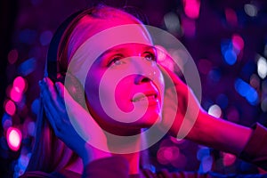 Happy young blonde woman listens to music with headphones in a nightclub.