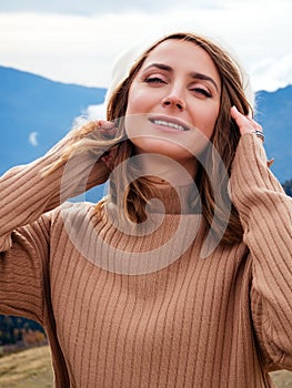 Happy young blonde woman looking at camera and smiling with teeth. Portrait of a beautiful girl in the mountains. Hair blowing