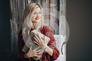 Happy young blonde woman in a red sweater received a gift for Christmas, new year, the girl smiles and holds a gift box