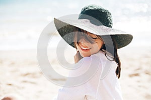 Happy young boho woman in hat relaxing and enjoying sunny warm day at ocean. Space for text. Stylish hipster girl sitting on beach