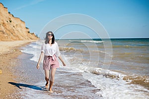 Happy young boho woman running and smiling in sea waves in sunny warm day on tropical island. Summer vacation. Space for text.