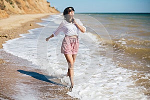 Happy young boho woman running and smiling in sea waves in sunny warm day on tropical island. Summer vacation. Space for text.