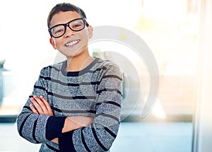 Happy, young boy and arms crossed with glasses for eye care and optometry indoor at home with lens flare. Smile, male