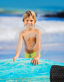 Happy young boy at the beach with surfboard