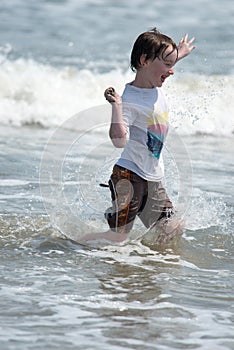 A happy young boy child running playing and having fun in the surf and waves of a sandy sunny beach