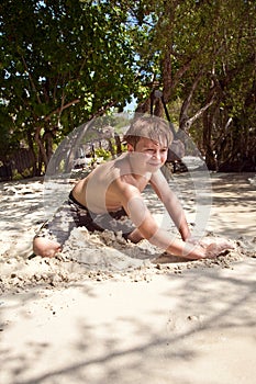 Happy young boy is digging at the beach