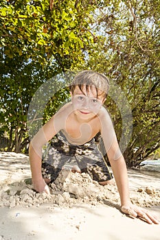 Happy young boy is digging in the sand of the beach