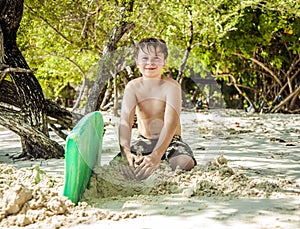 Happy young boy is digging in the sand of the beach