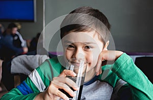 Happy young boy drinking glass of cold drink, Portrait Child with smiling face sitting in cafe drinking soda or soft drink,