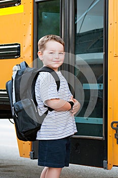 Happy young boy in front of school bus