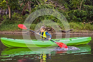 Happy young boy holding paddle in a kayak on the river, enjoying a lovely summer day