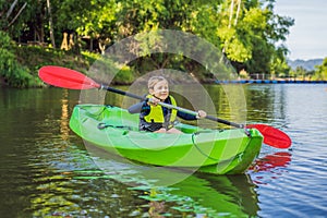 Happy young boy holding paddle in a kayak on the river, enjoying a lovely summer day
