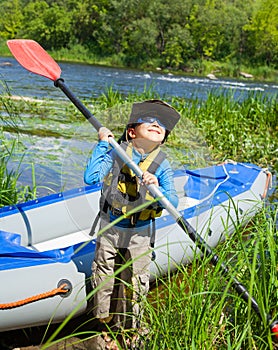 Happy young boy holding paddle near a kayak