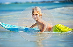 Happy young boy in the ocean on surfboard