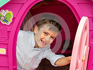 Happy young boy playing in the plastic house in the garden