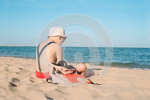 Happy young boy reading a book on a sunny dayl. boy sitting Sad with his back at the beach. Last day of vacation. Back to school.