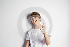 Happy young boy in white T-shirt posing in front of white empty wall. Portrait of fashionable male child. Smiling boy