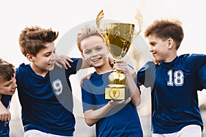 Happy young boys in sports team winning a soccer-football game and holding a golden trophy. Kids soccer players celebrate a