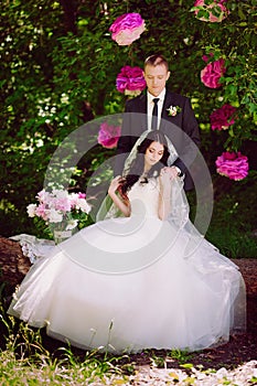 Happy young bride and groom in a pink decorated with peonies area in nature, family, relationships, romance, smiles, hugs, love