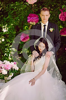 Happy young bride and groom in a pink decorated with peonies area in nature, family, relationships, romance, smiles, hugs, love