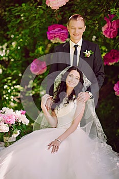 Happy young bride and groom in a pink decorated with peonies area in nature, family, relationships, romance, smiles, hugs, love