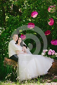 Happy young bride and groom in a pink decorated with peonies area in nature, family, relationships, romance, smiles, hugs, love