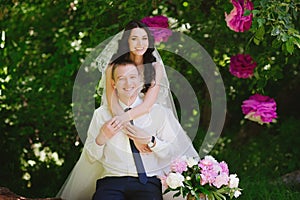 Happy young bride and groom in a pink decorated with peonies area in nature, family, relationships, romance, smiles, hugs, love