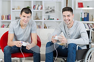 happy young brothers playing video games one on wheelchair