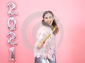 Young woman on a pink background with silver ballons in the form of the numbers 2021 photo