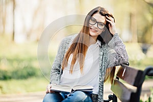 Happy young brunette with a notebook in hands sitting on a park bench