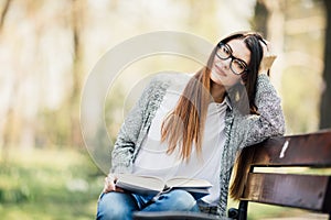 Happy young brunette with a notebook in hands sitting on a park bench