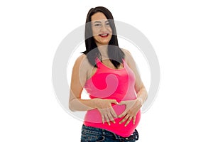 Happy young brunette pregnant girl in pink shirt with hand on her belly posing isolated on white background