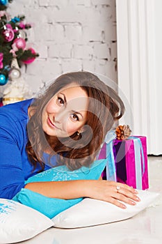 Happy young brunette woman with gift box near christmas tree. X-mas or New Year tree concept.