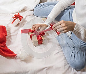 Happy young brunette woman in santa claus hat opens a gift box for Christmas lying on a white bed. Christmas gifts.