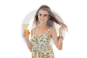 Happy young brunette woman in sarafan with floral pattern drinks orange cocktail and smiling on camera isolated on white